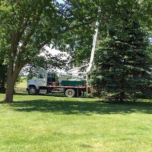 Green and white Waskosky Well Drilling truck being used for work in a backyard with trees.